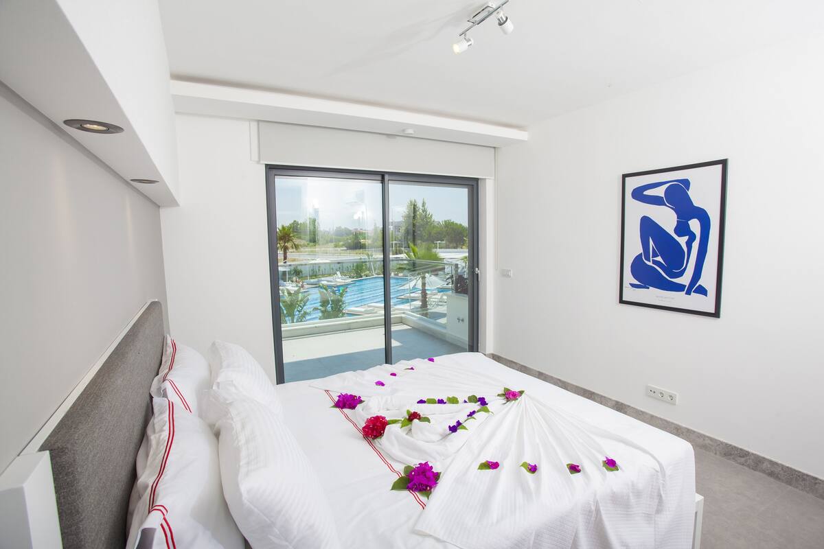 Quarto de hotel com uma cama, uma janela grande e uma obra de arte emoldurada na parede.