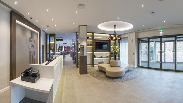 A modern hotel lobby with a reception desk, seating area, and a large glass door entrance. - Hilton Garden Inn Manchester Emirates Old Trafford (Manchester)