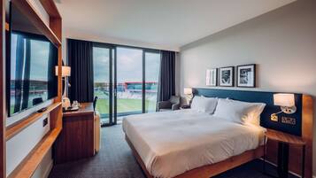 Une chambre d’hôtel avec un grand lit, un bureau, une chaise et une vue sur un stade par la fenêtre.