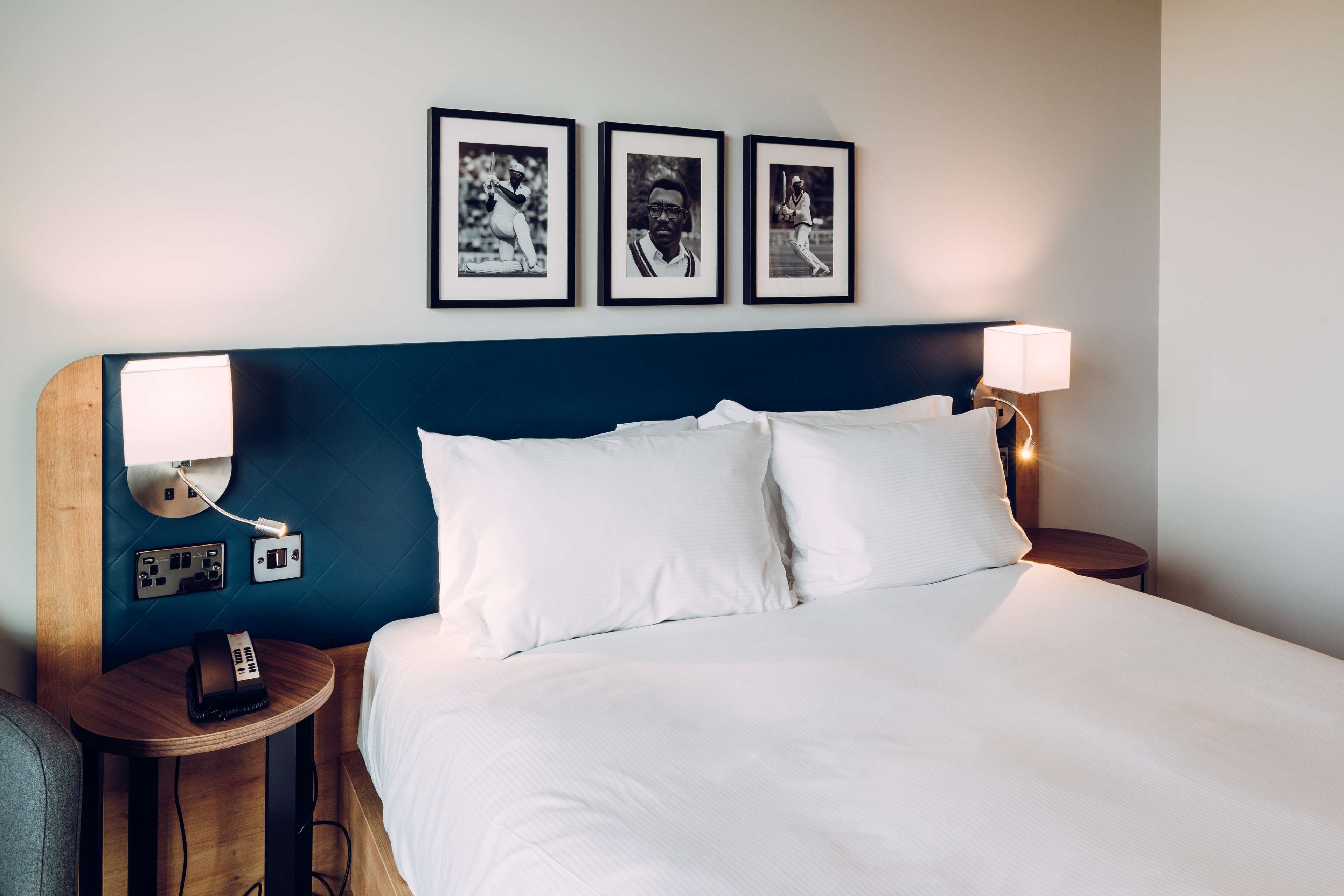 A neatly made bed with white linens, a wooden headboard, and a wall-mounted light fixture.