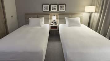 Quarto de hotel com duas camas de solteiro, uma mesa de cabeceira com abajur e três quadros na parede.
