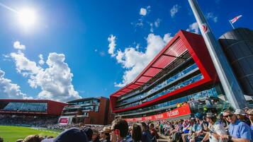 Un stade rempli d’une foule nombreuse, un ciel dégagé et un bâtiment imposant aux couleurs rouge et blanche.