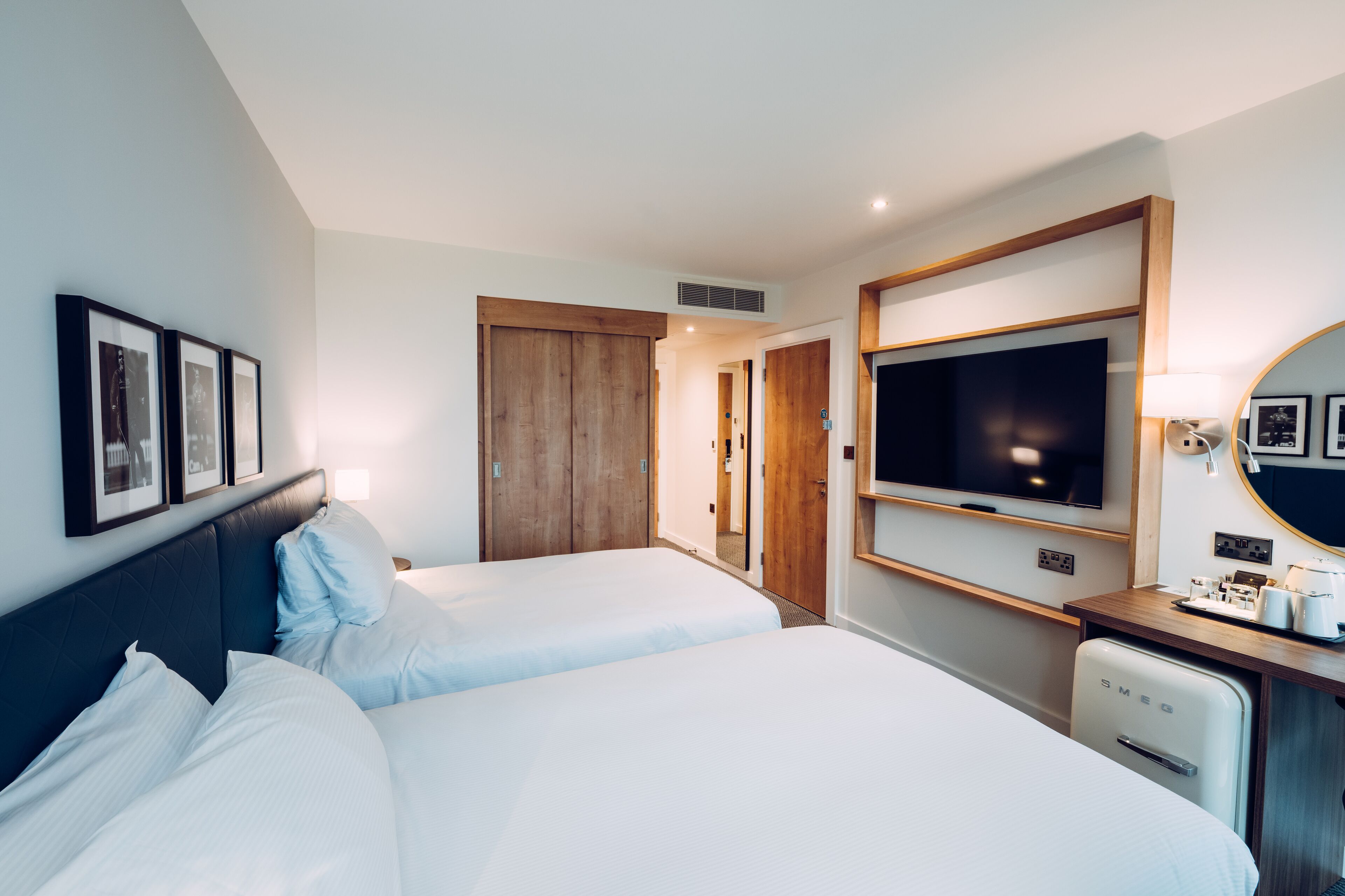 A hotel room with two beds, a TV, a small fridge, and a mirror.