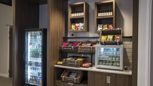 A beverage vending area with a refrigerator and shelves stocked with bottled water, soda, and snacks. - Hilton Garden Inn Manchester Emirates Old Trafford (Manchester)