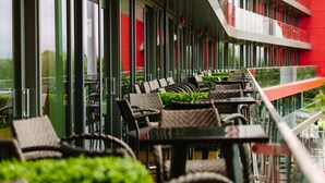 An outdoor seating area with wicker chairs and tables, a glass railing, and a red building in the background. - Hilton Garden Inn Manchester Emirates Old Trafford (Manchester)
