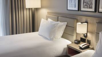 A hotel room with a bed, bedside lamp, alarm clock, and framed pictures on the wall.