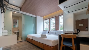 A modern hotel room with a bed, a desk, and a view of buildings through large windows. - The Period Pratunam (Bangkok)
