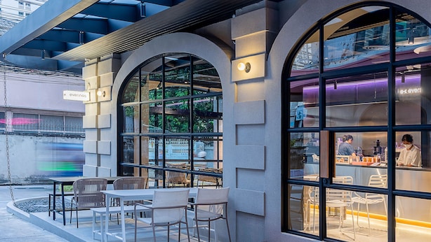 An outdoor seating area with tables and chairs, large windows, and a view of the street. - The Period Pratunam (Bangkok)