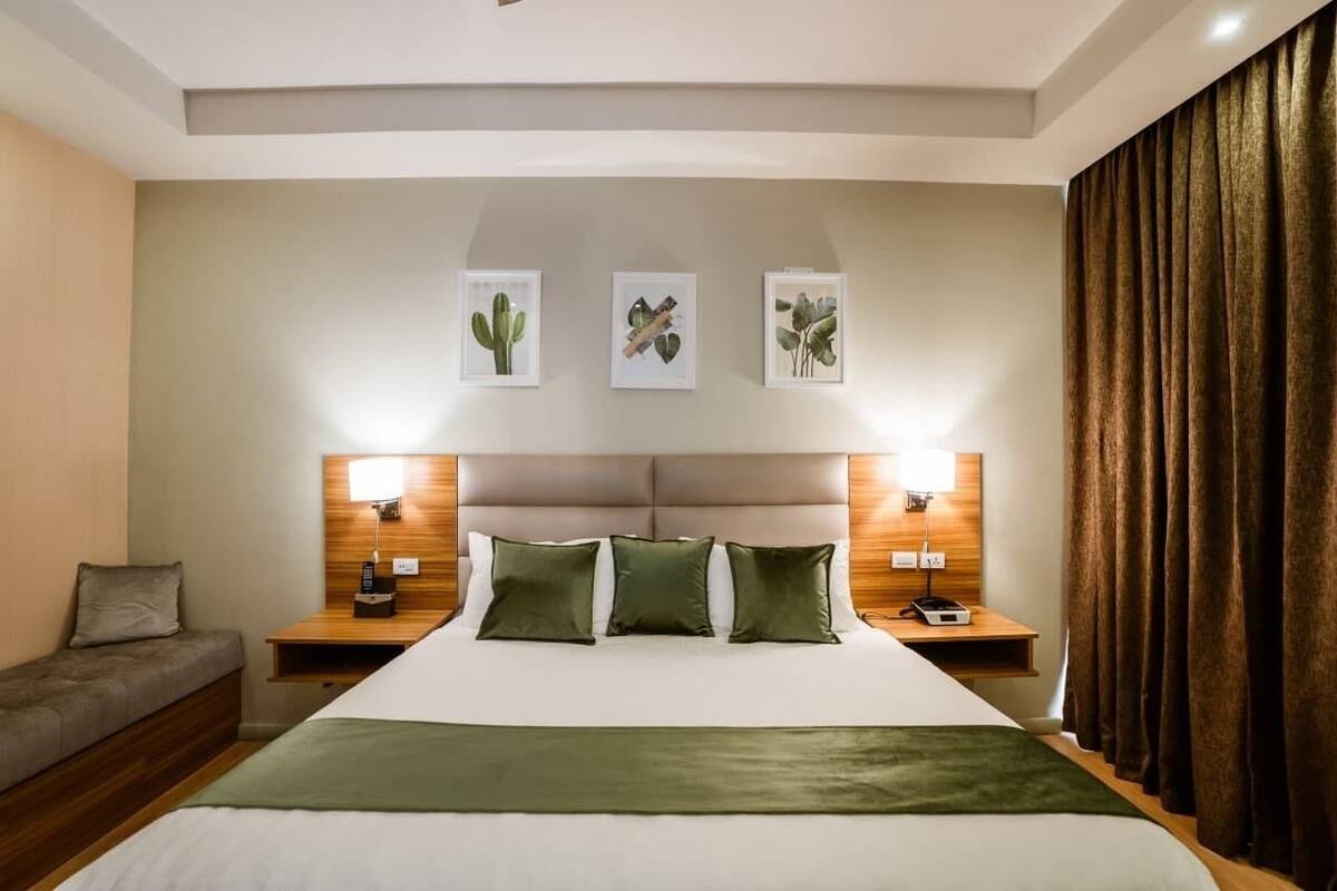 A hotel room with a large bed, two bedside tables, a nightstand, a sofa, and a headboard with wall art.