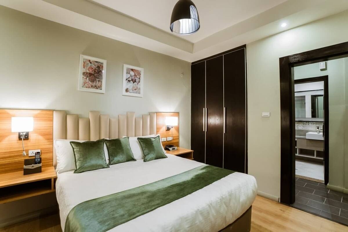 A hotel room with a bed, bedside lamps, a wardrobe, and a mirror.