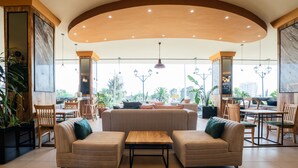 A spacious indoor area with a high ceiling, a central seating area with sofas and a coffee table, and a dining area with chairs and tables. - Monarch Hotel (Addis Ababa)