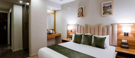 Een hotelkamer met een groot bed, een houten hoofdeinde, een nachtkastje met een lamp en een aan de muur hangend schilderij.