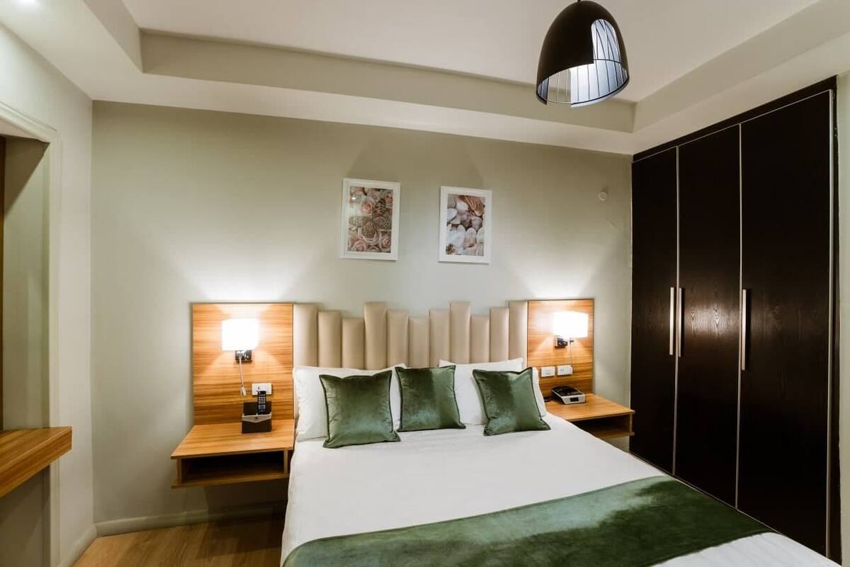 A hotel room with a large bed, two bedside tables with lamps, a wardrobe, and two framed pictures on the wall.