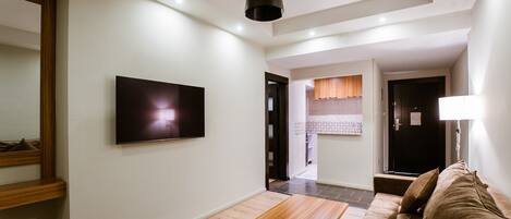 Una sala de estar moderna con televisor de pantalla plana, una mesa de centro de madera, un sofá marrón y una lámpara colgante.