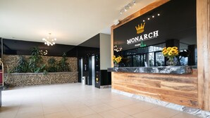 A modern hotel lobby with a reception desk, a stone wall with plants, and a large window. - Monarch Hotel (Addis Ababa)