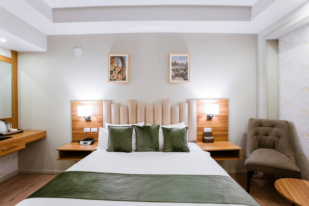 A hotel room with a large bed, two bedside tables, a chair, and two wall-mounted lamps.
