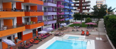 Una piscina al aire libre, sombrillas, sillones reclinables de piscina