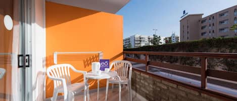 Un balcon avec des chaises en plastique blanches et une petite table, une enseigne indiquant «
eó Hotels
», et une vue sur des bâtiments en arrière-plan.