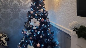 Un árbol de Navidad decorado con luces y adornos, una araña de cristal y una pared con papel pintado estampado.