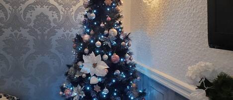 Un sapin de Noël décoré de guirlandes lumineuses et d’ornements, un lustre et un mur recouvert d’un papier peint à motifs.
