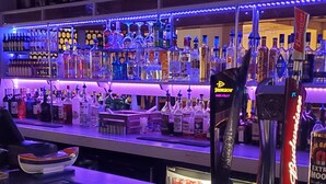 Una zona de bar con estantes de botellas de licor, una barra con un teclado y un letrero de neón.