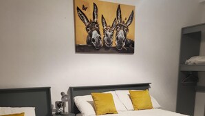 Habitación de hotel con dos camas, cada una con almohadas blancas y color mostaza, un cuadro de burros en la pared y un escritorio pequeño con una lámpara.