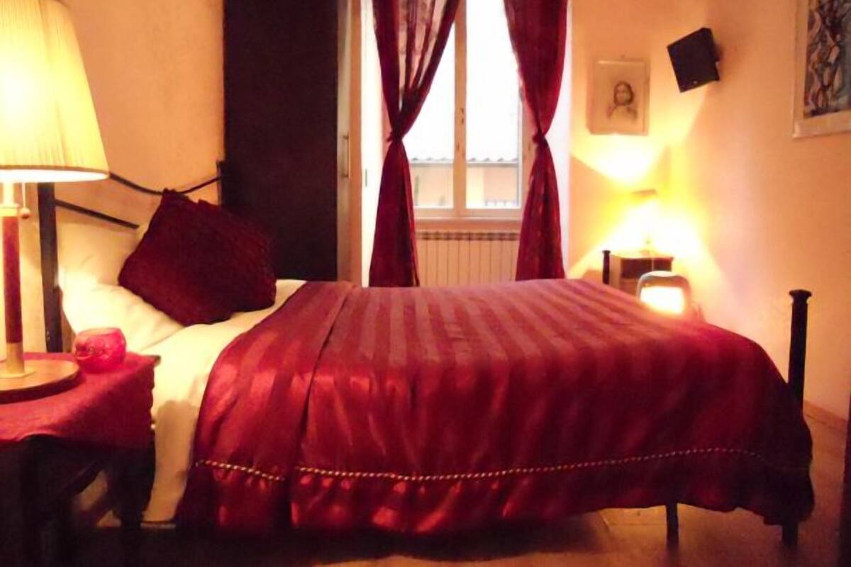 A hotel room with a bed, a nightstand, a lamp, a window with curtains, and a framed picture on the wall.