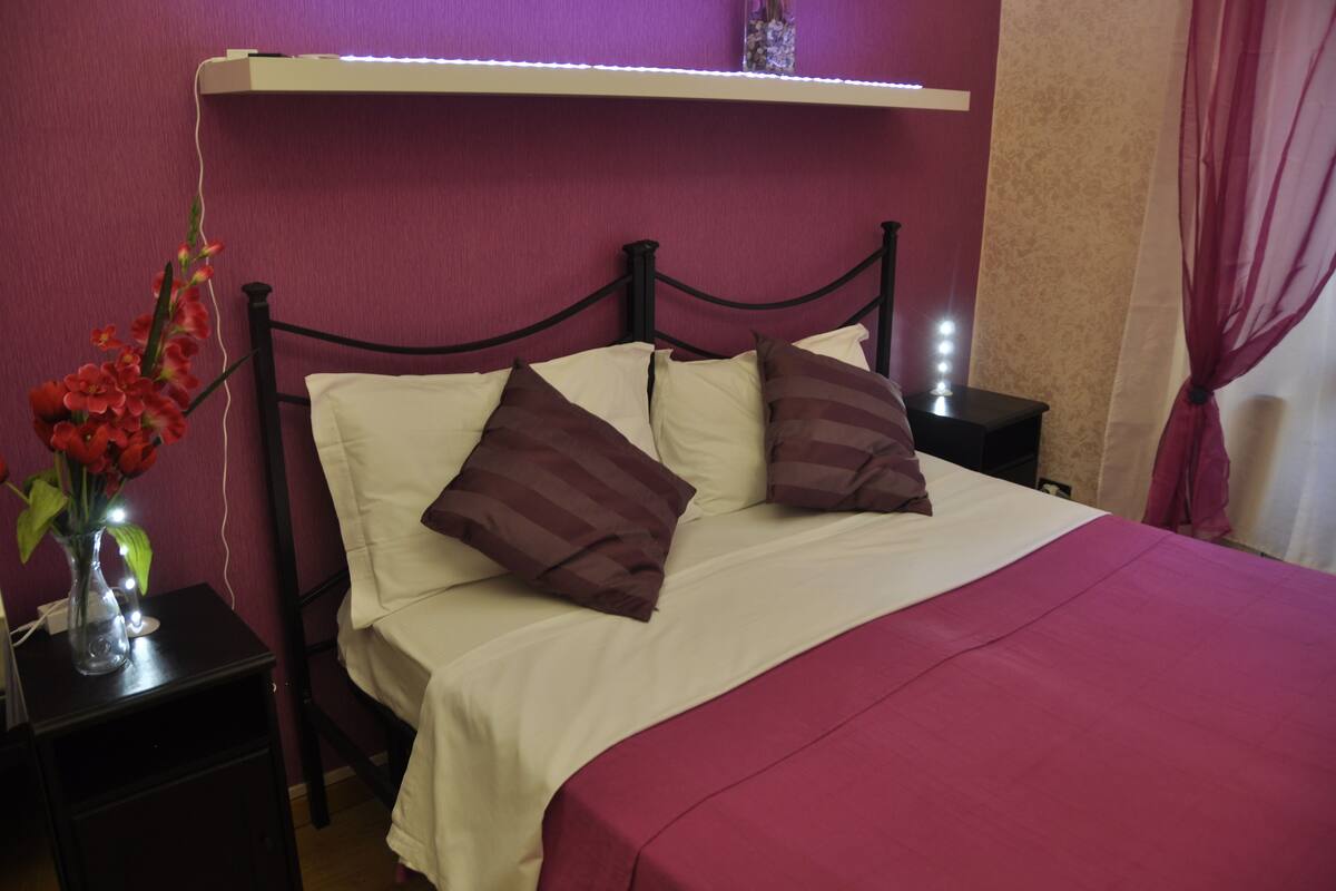 A bed with white and brown bedding, a vase with flowers, and a nightstand with a lamp.
