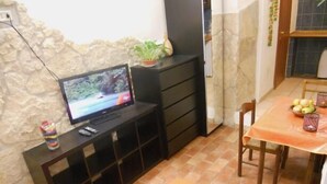 A living room with a television on a black stand, a dining table with chairs, and a tiled floor. - Belhorizon Guest House (Rome)