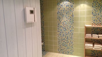 Ein Badezimmer mit Duschbereich, gefliesten Wänden, Ablagefläche für Handtücher und einer Bedienkonsole.