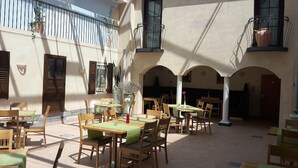An outdoor patio with multiple tables and chairs, surrounded by arches and balconies with plants. - EuroStar Hotel (Castrop-Rauxel)
