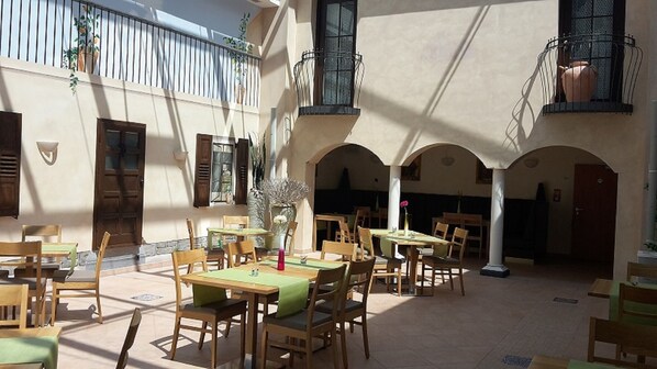 An outdoor patio with multiple tables and chairs, surrounded by arches and balconies with plants. - EuroStar Hotel (Castrop-Rauxel)