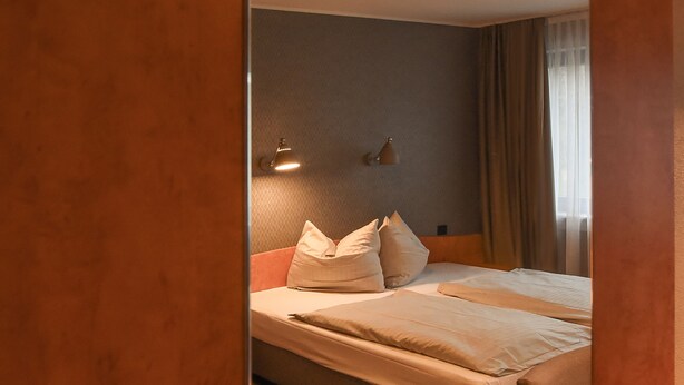 A hotel room with a bed, a chair, a nightstand, and a lamp. - EuroStar Hotel (Castrop-Rauxel)