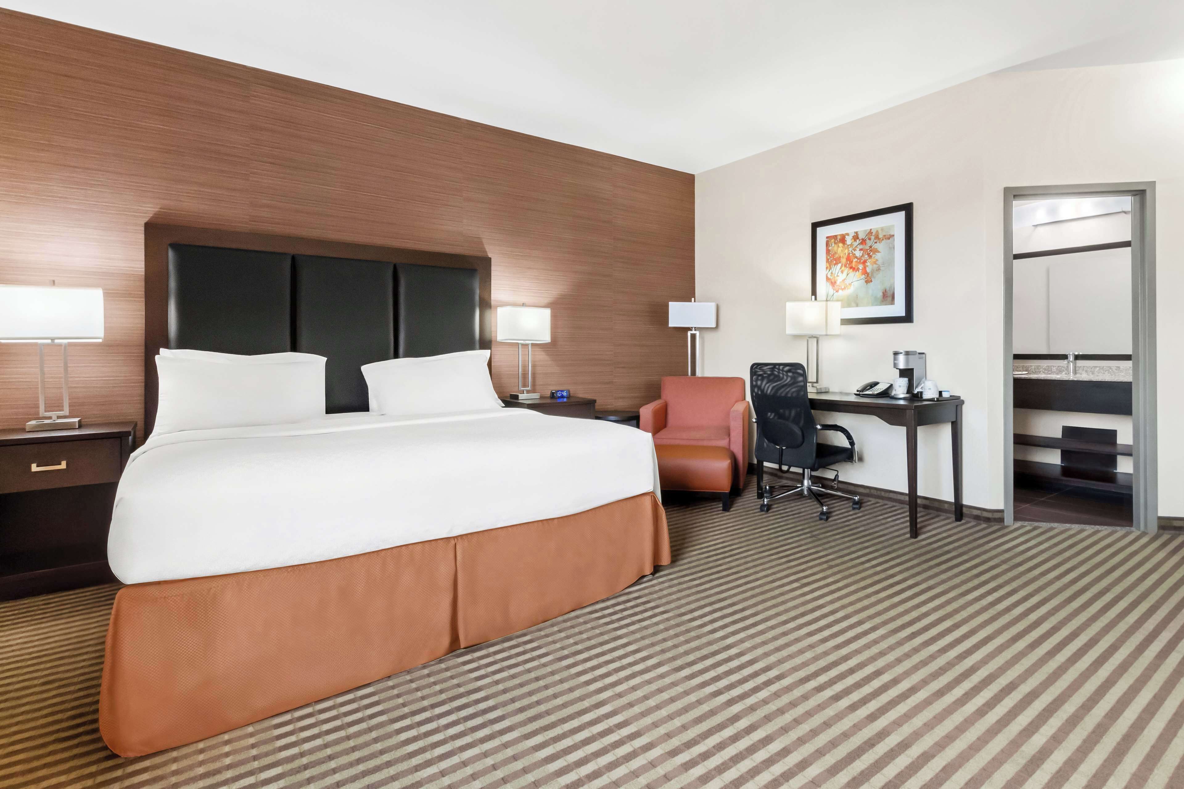 Habitación de hotel con una cama grande, un escritorio con una silla, una lámpara de escritorio, un teléfono y un cuadro en la pared.