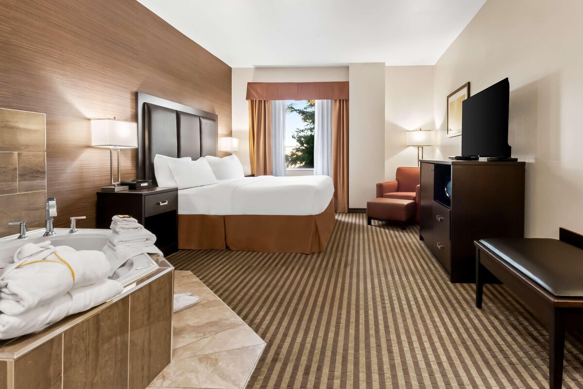 Habitación de hotel con cama, escritorio, televisor, baño con bañera y ventana con cortinas.