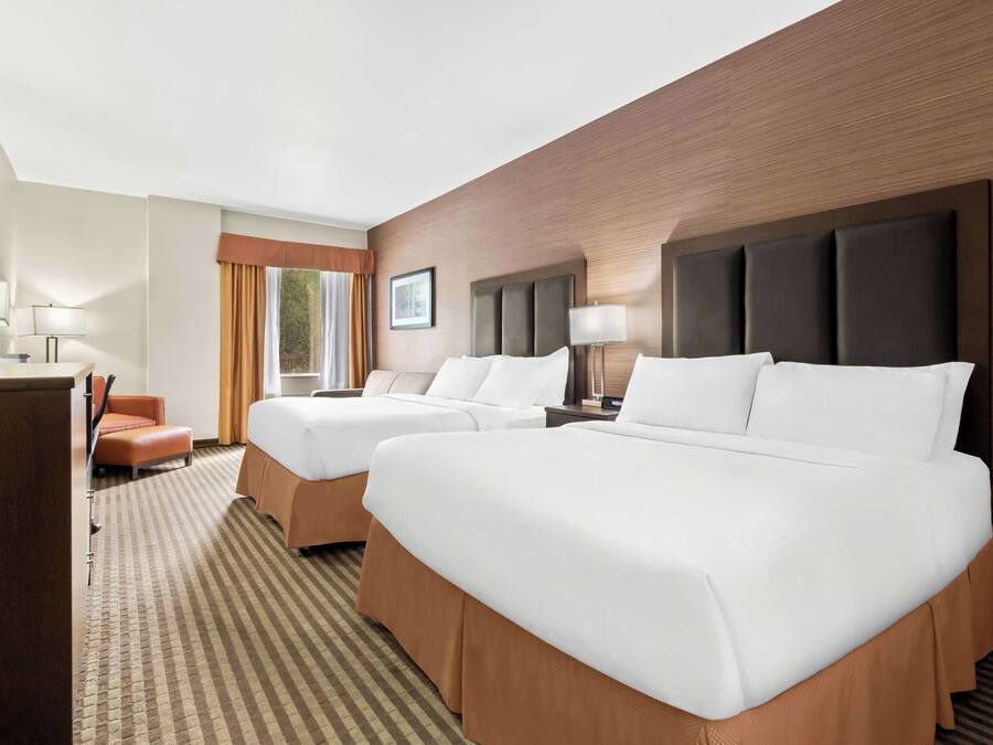 A hotel room with two beds, a desk, a chair, and a television.