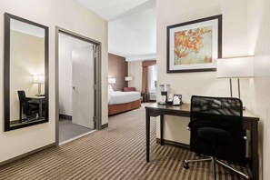 Habitación de hotel con cama, escritorio con silla, cafetera y un cuadro en la pared.