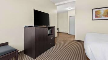 A hotel room with a bed, a TV on a wooden cabinet, a small desk, and a framed picture on the wall.