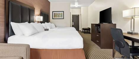 A hotel room with a large bed, a desk, a chair, a television, and a lamp.