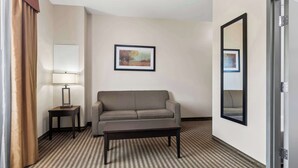 Una camera d'albergo con un divano, un tavolino con una lampada, un quadro appeso al muro e uno specchio.