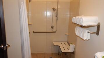 A shower area with a glass door, a towel rack with folded towels, and a grab bar.