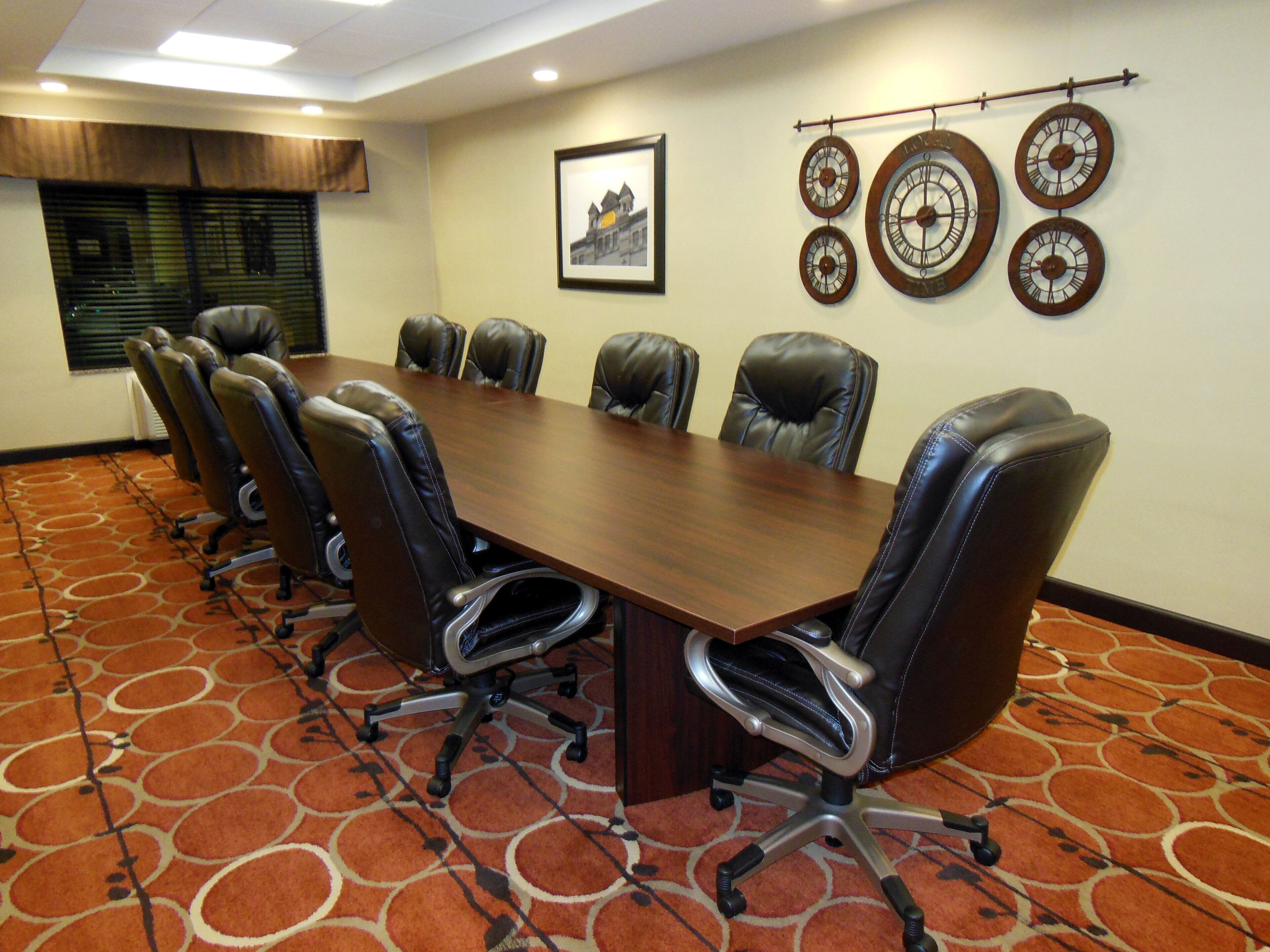 Une salle de conférence avec une longue table, des fauteuils en cuir, une horloge au mur et un tableau encadré.