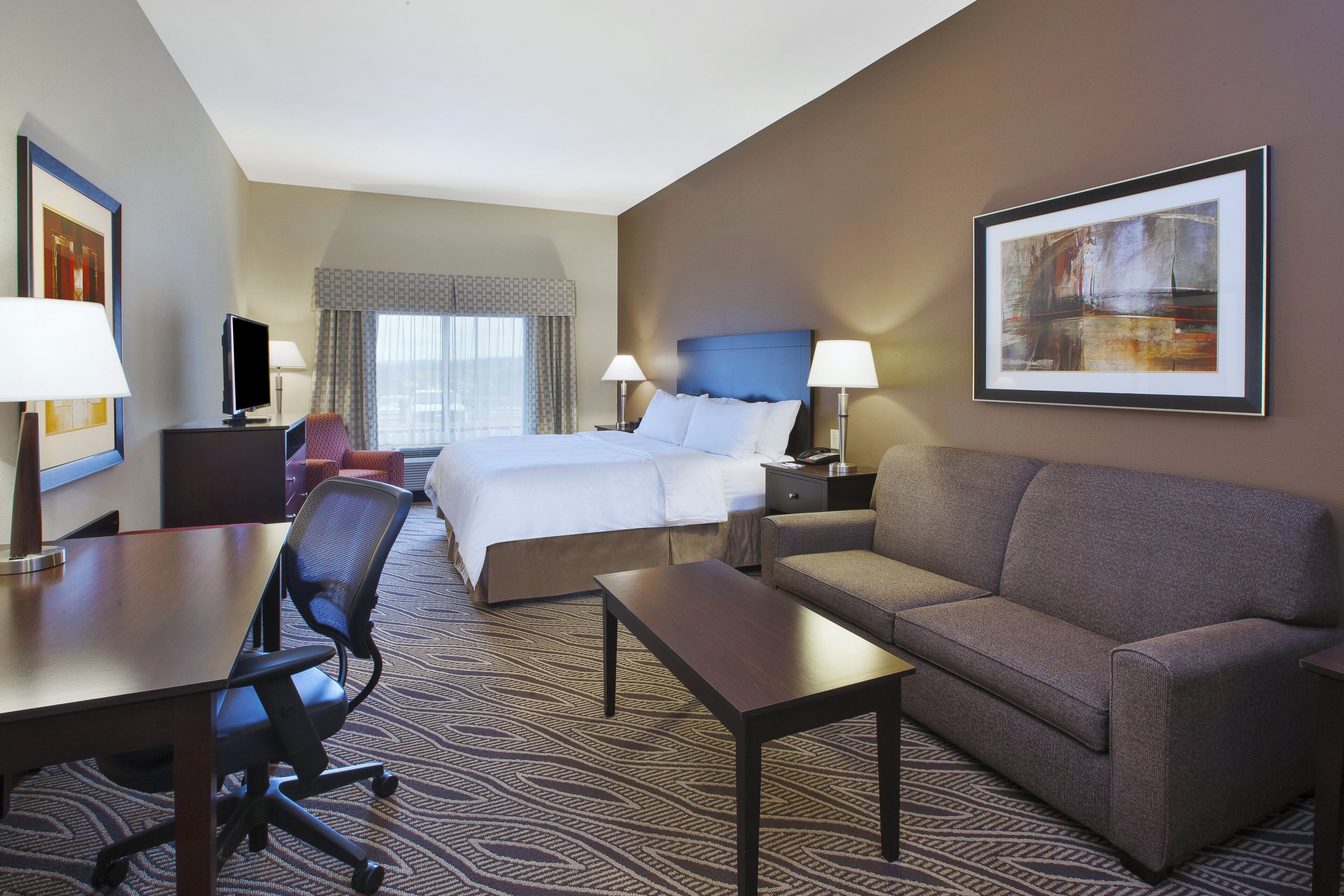 A hotel room with a bed, a sofa, a desk, a chair, and a television.