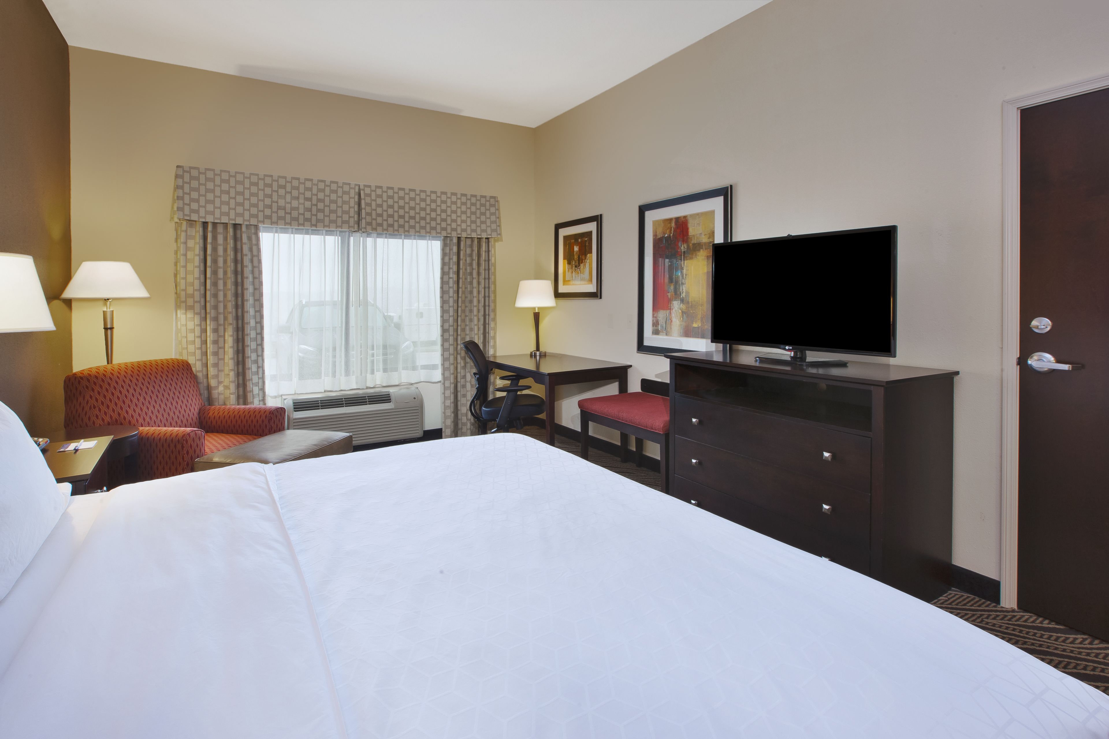 A hotel room with a large bed, a desk with a chair, a television, and a door.