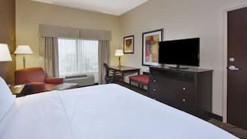 A hotel room with a large bed, a desk with a chair, a television, and a door.
