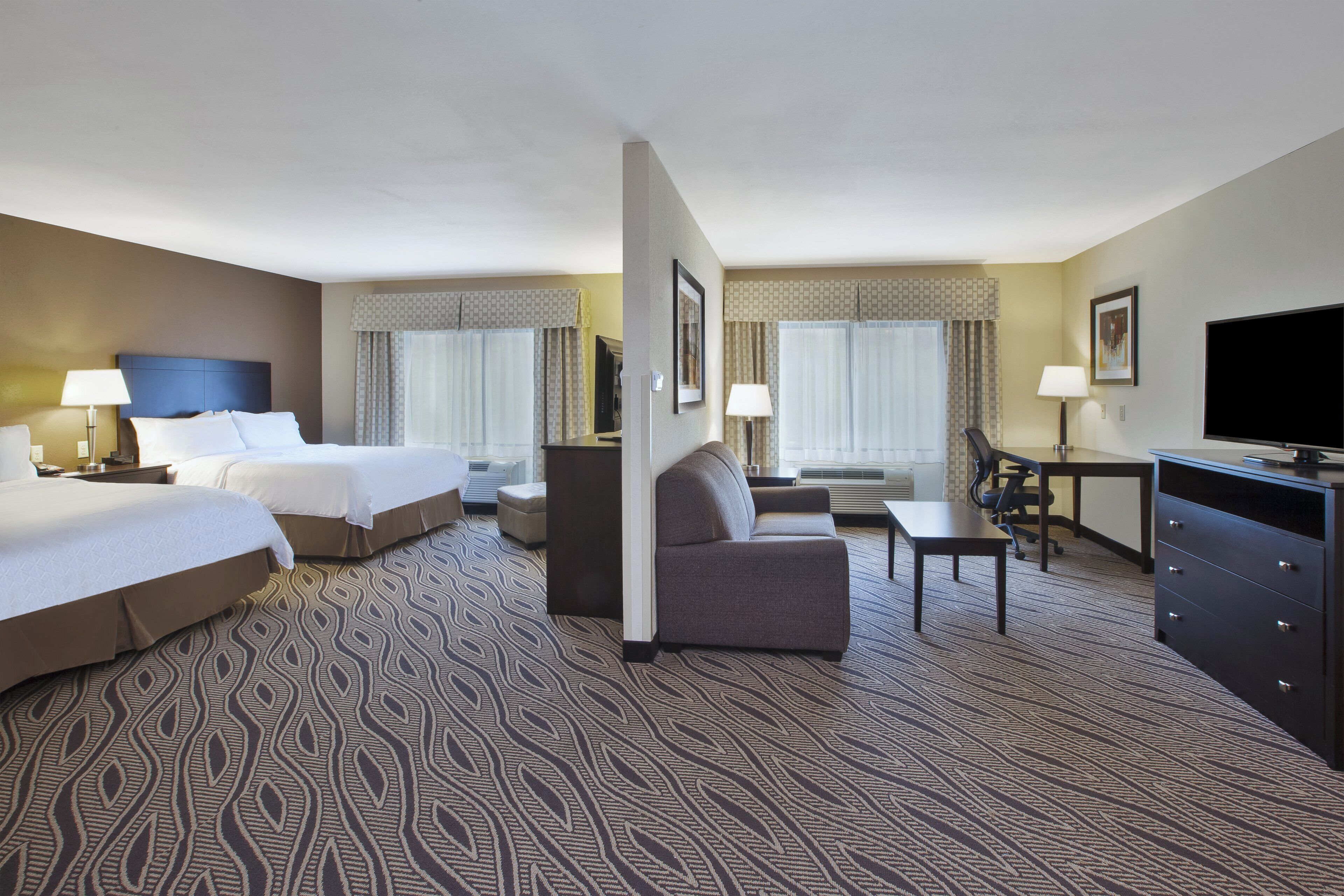 A hotel room with two beds, a desk, a chair, a television, and a patterned carpet.