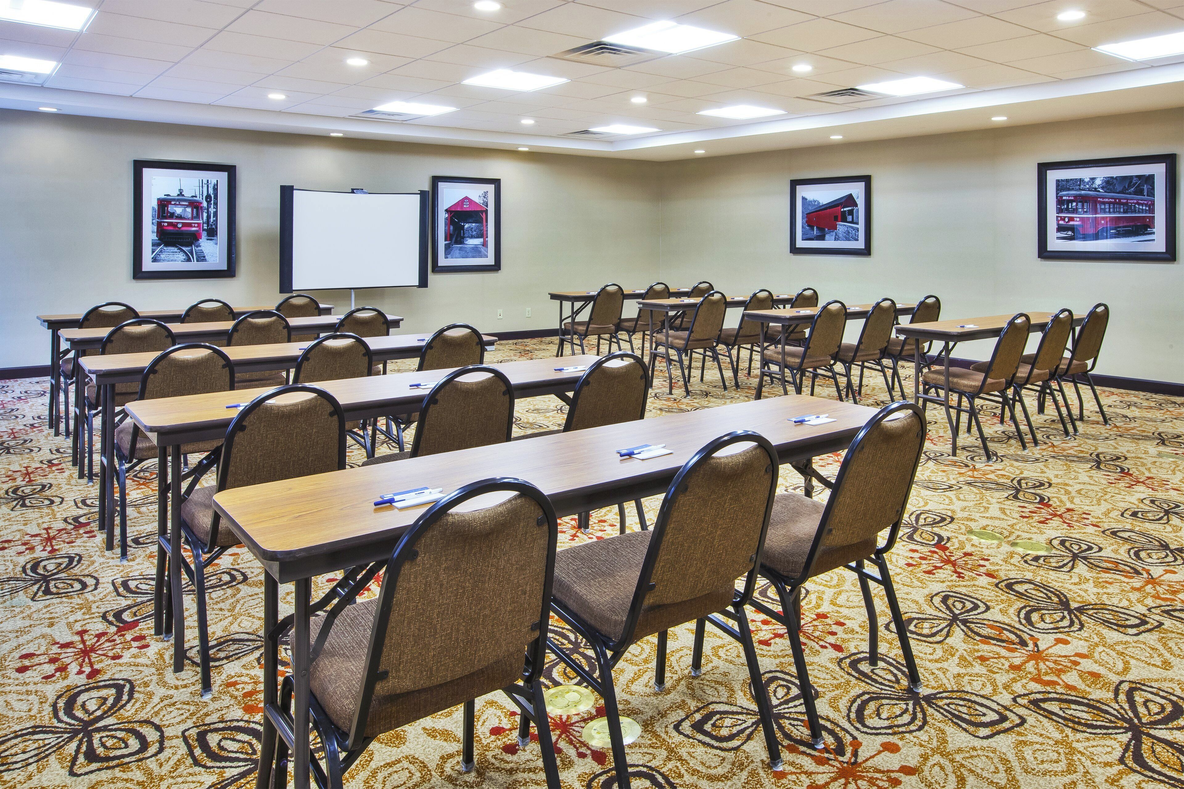 A conference room with multiple tables and chairs, a whiteboard, and framed pictures on the walls.