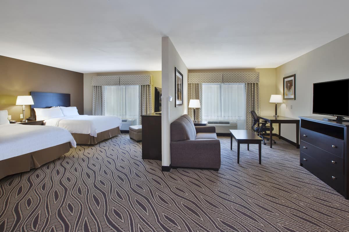 A hotel room with two beds, a sofa, a desk, and a TV.