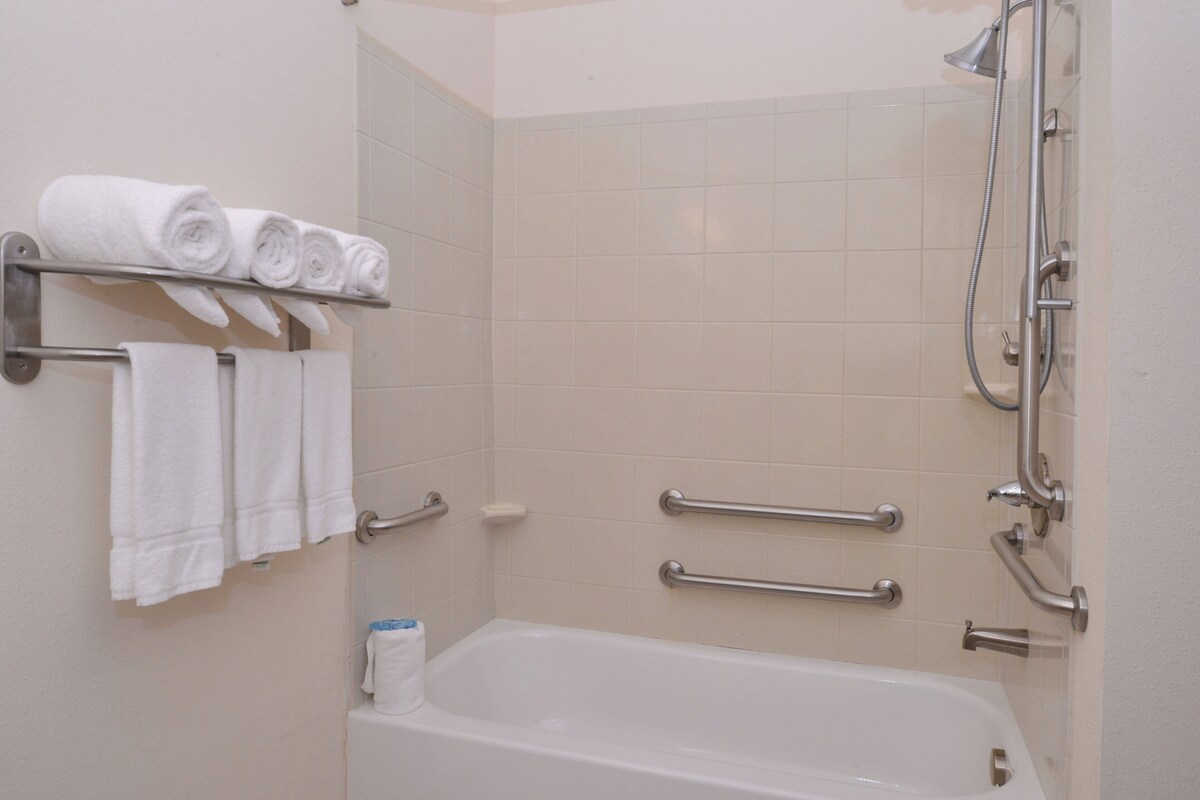 Een badkamer met een bad, een handdoekhouder met opgerolde handdoeken en een douche met een handdouche.