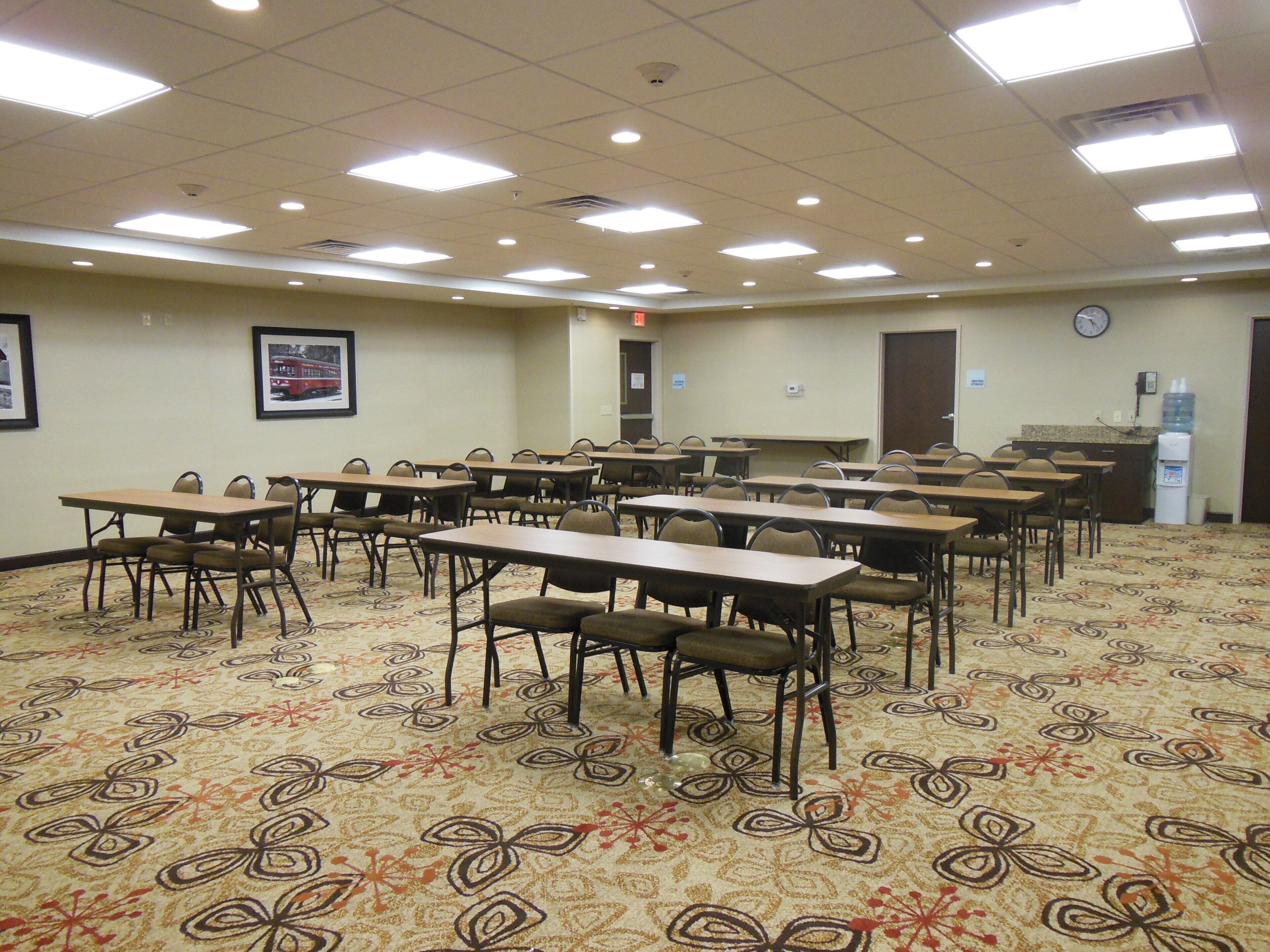 A conference room with multiple tables and chairs, a clock on the wall, and a water dispenser.